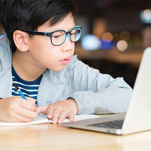 young boy taking notes from laptop