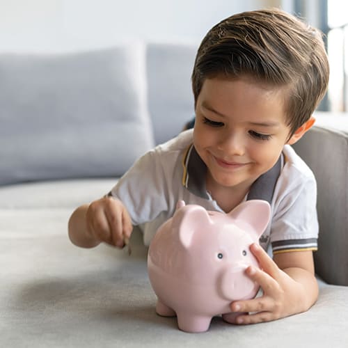young boy putting coins in piggy bank